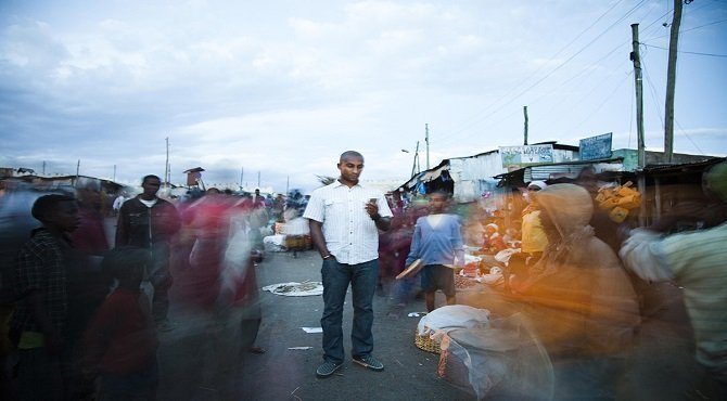 A young Ethiopian man stands in a crowded city market in an impoverished neighborhood of Harar, Ethiopia while checking his email/African Business